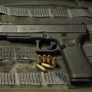 Glock 34 Gen 5 MOS long-slide pistol side profile resting on a bullet vest backgound with 9mm alongside