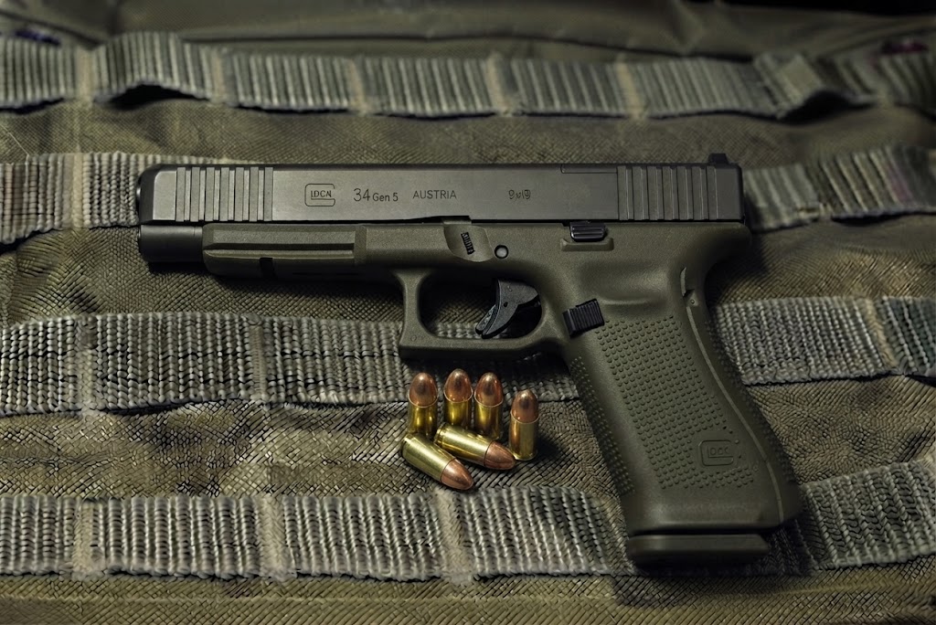Glock 34 Gen 5 MOS long-slide pistol side profile resting on a bullet vest backgound with 9mm alongside