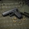 Glock 22 Gen 3 .40 S&W pistol side profile resting on a neutral background along side it case and some 9mm luger bullets